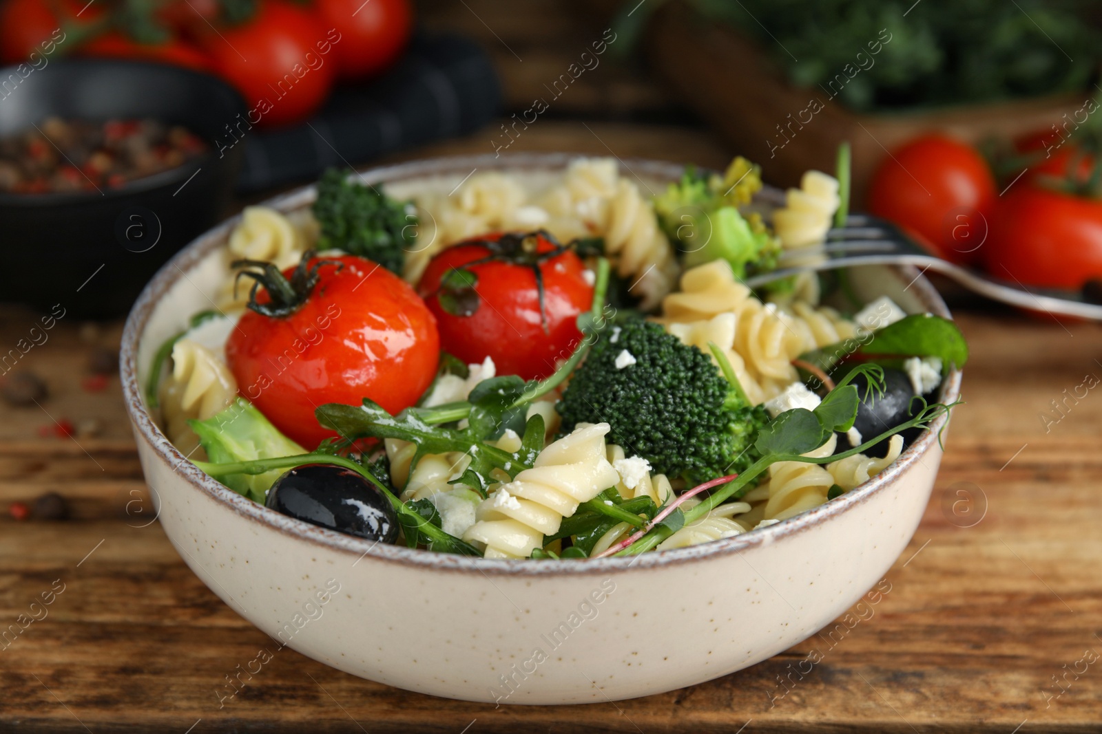 Photo of Bowl of delicious pasta with tomatoes, broccoli and cheese on wooden table, closeup