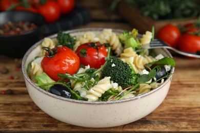 Bowl of delicious pasta with tomatoes, broccoli and cheese on wooden table, closeup