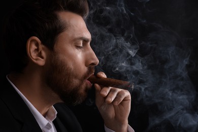 Photo of Handsome man smoking cigar on black background. Space for text