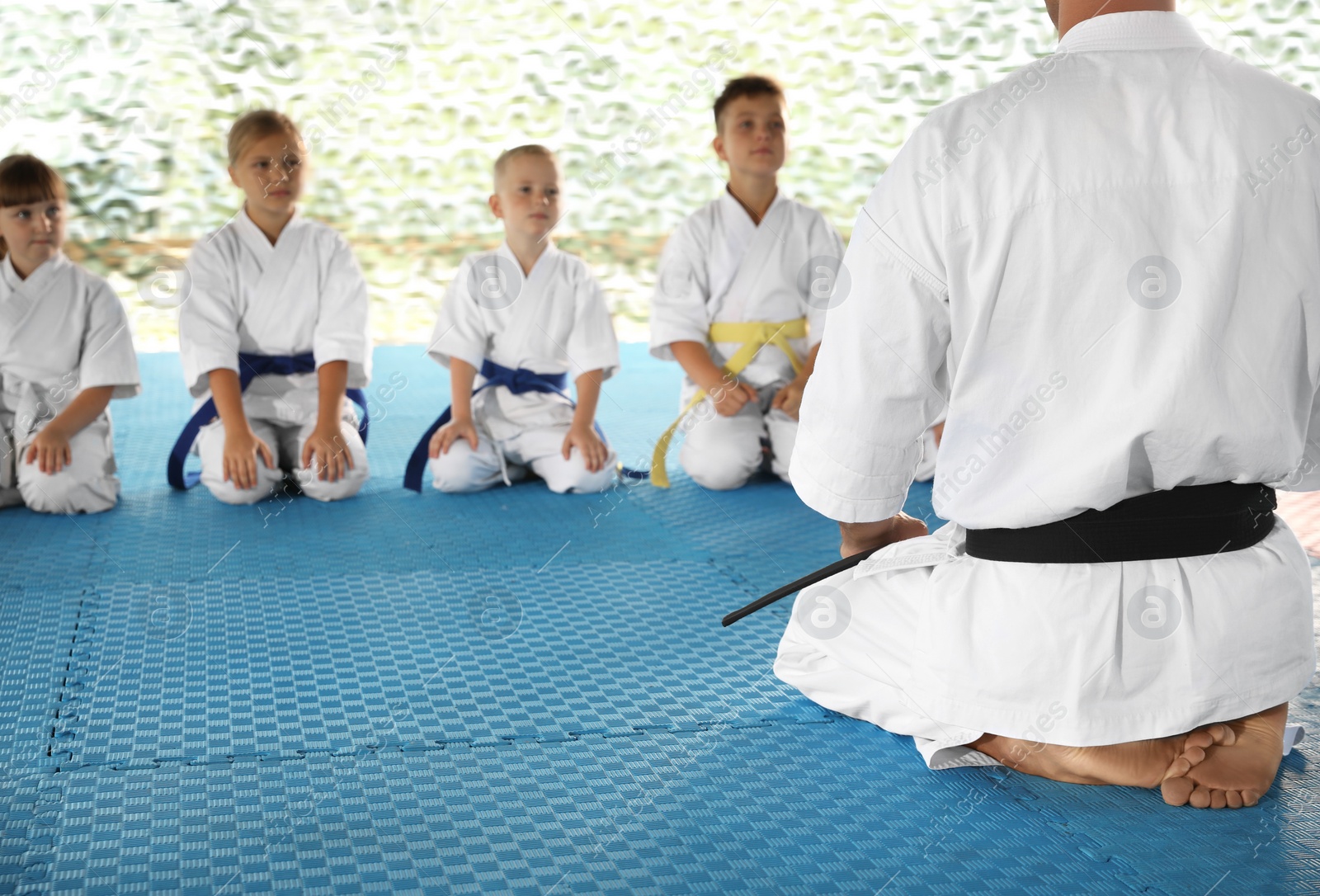 Photo of Children and coach sitting on tatami outdoors. Karate practice