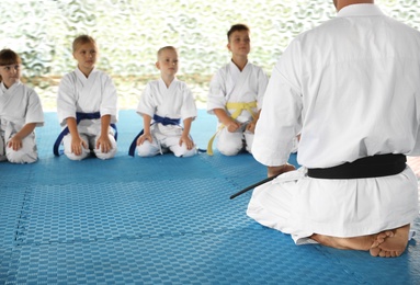 Photo of Children and coach sitting on tatami outdoors. Karate practice