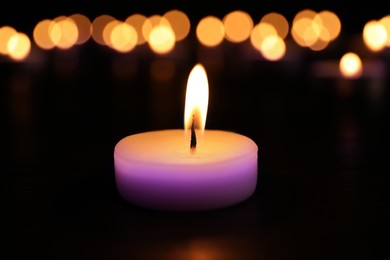 Burning violet candle on dark surface. Funeral attributes