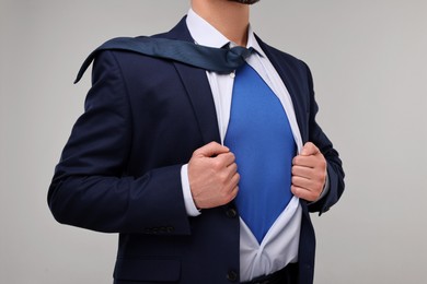 Photo of Businessman wearing superhero costume under suit on beige background, closeup