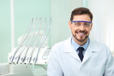 Professional male dentist in white coat at workplace. Space for text