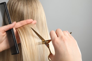 Hairdresser cutting client's hair with scissors on light grey background, closeup