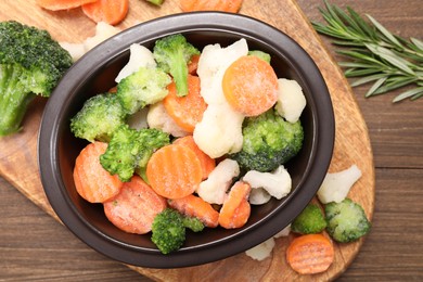 Mix of different frozen vegetables in bowl on wooden table, top view