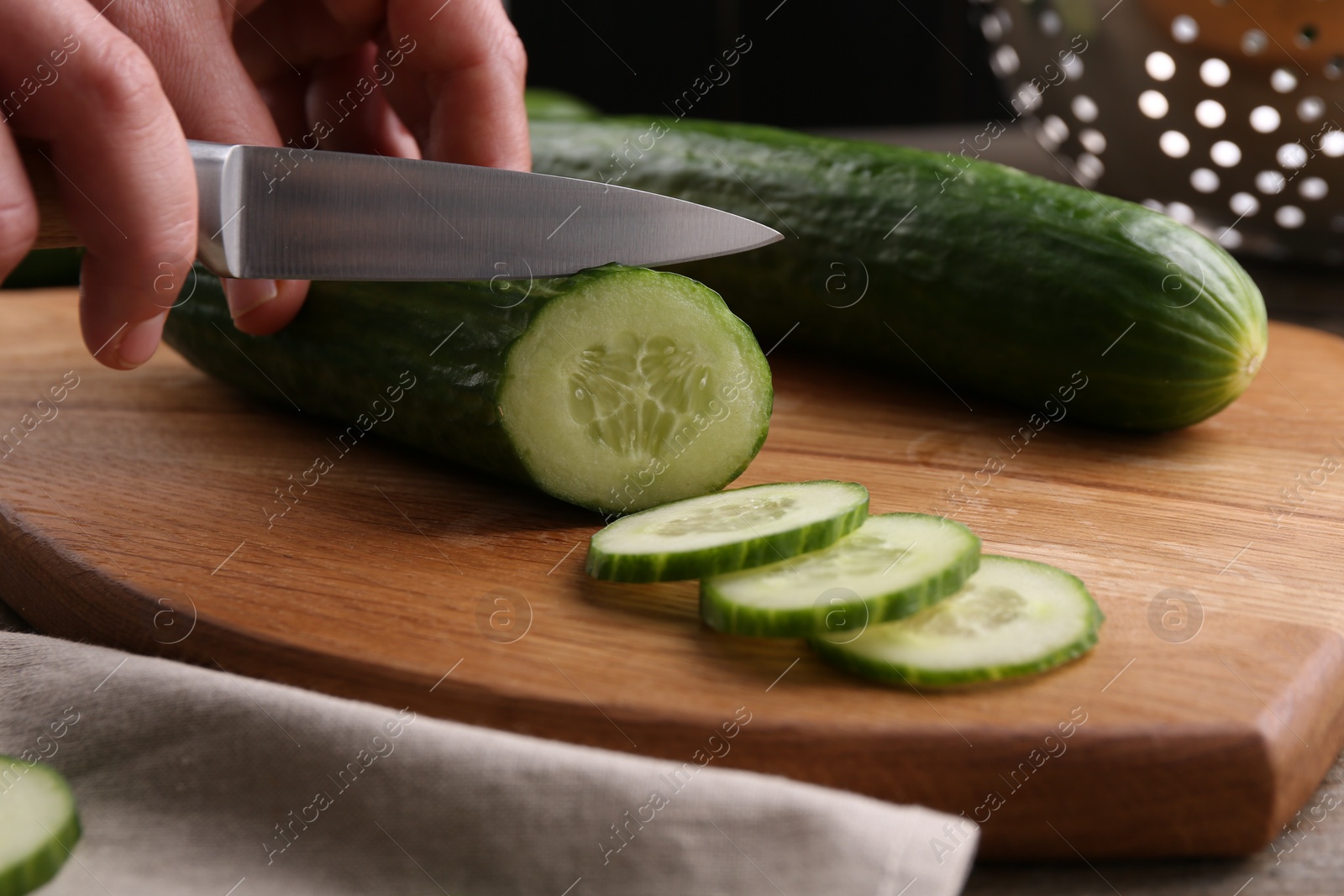 Photo of Woman cutting cucumber on wooden board at table, closeup