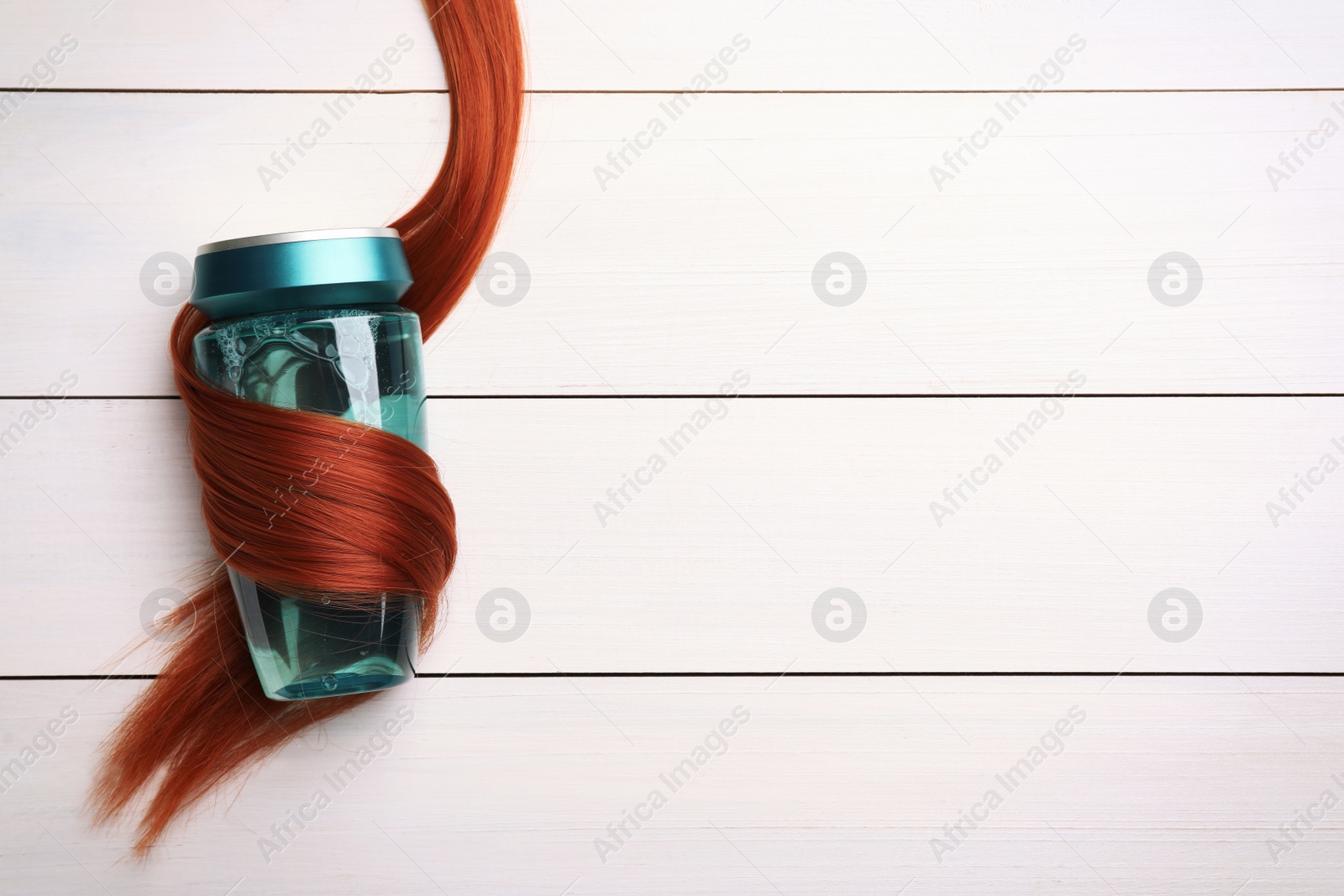 Photo of Bottle wrapped in lock of hair on white wooden background, top view with space for text. Natural cosmetic product