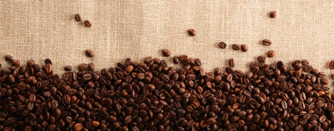 Photo of Many coffee beans on burlap fabric, top view. Space for text