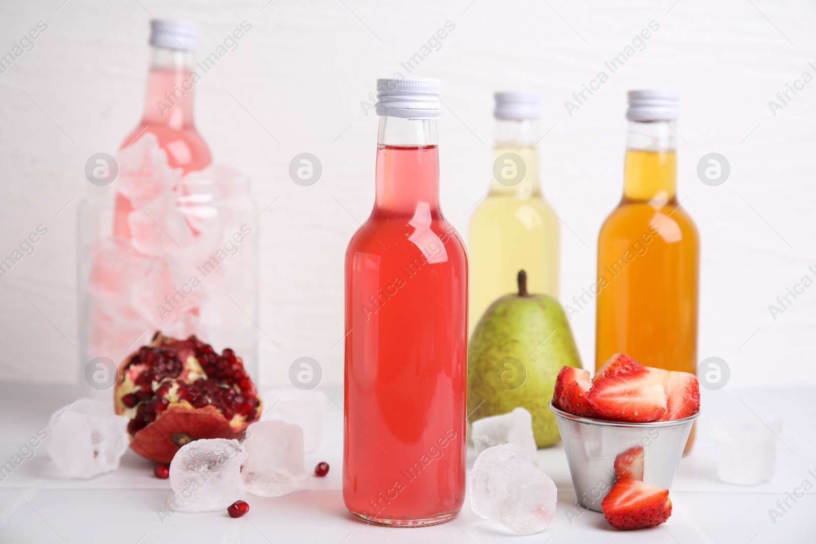 Photo of Tasty kombucha in glass bottles, fresh fruits and ice on white table