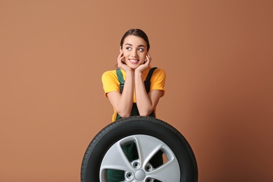 Female mechanic in uniform with car tire on color background
