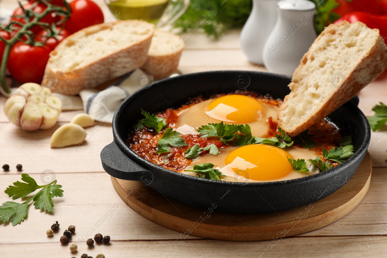 Photo of Delicious shakshuka with bread in frying pan on light wooden table, closeup