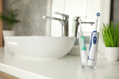 Photo of Electric toothbrushes in glass near vessel sink on bathroom vanity. Space for text