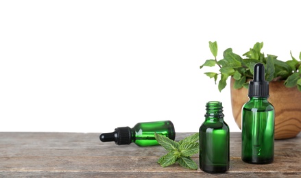 Bottles of mint essential oil on wooden table against white background. Space for text