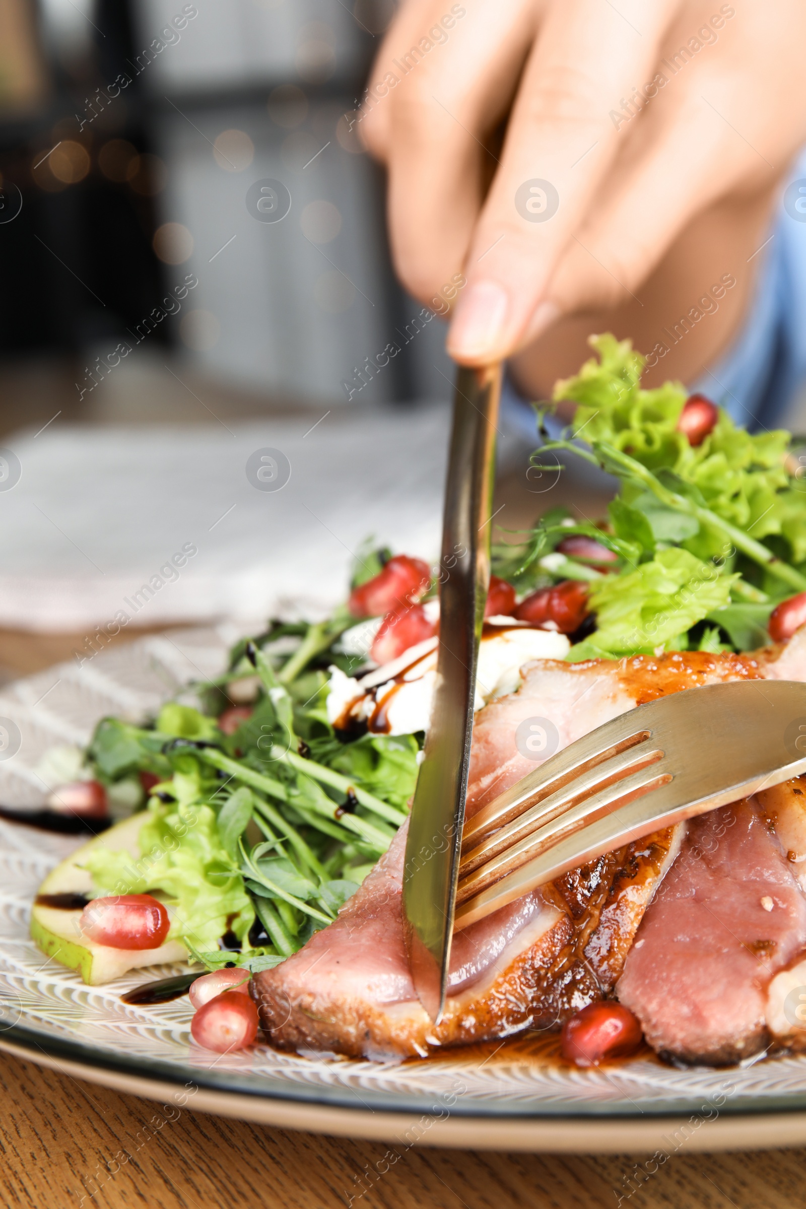 Photo of Woman eating delicious salad with roasted duck breast at wooden table, closeup