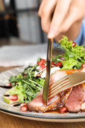 Photo of Woman eating delicious salad with roasted duck breast at wooden table, closeup