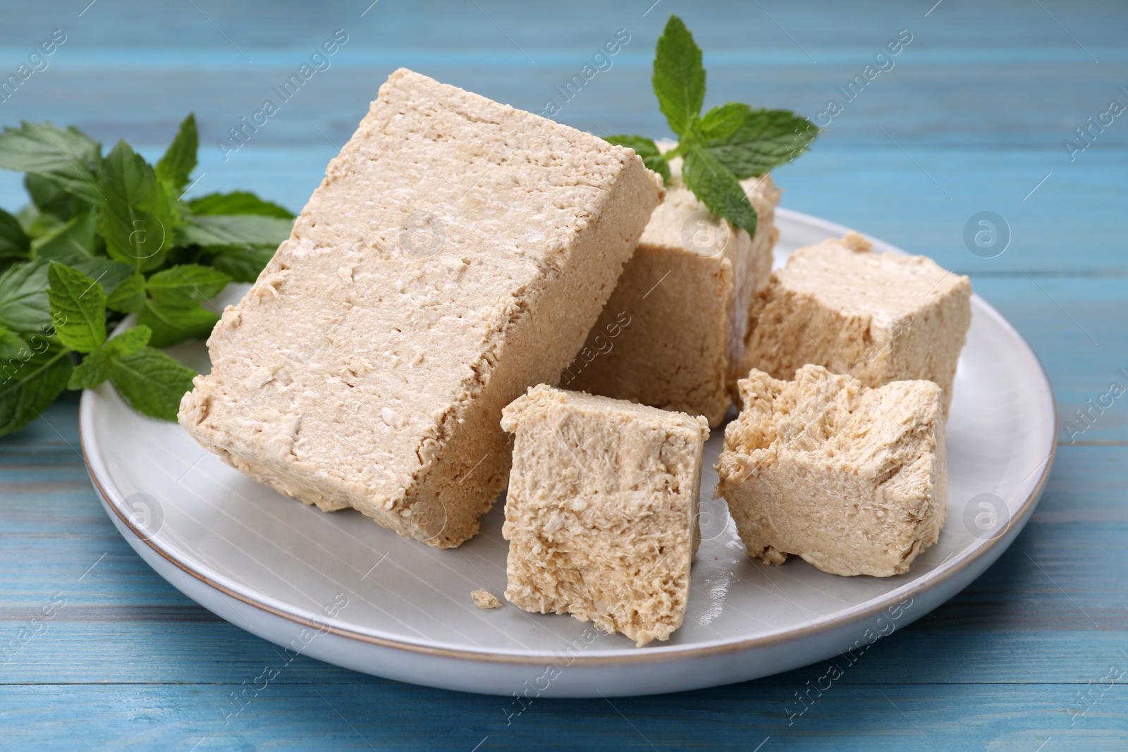 Photo of Pieces of tasty halva and mint on light blue wooden table, closeup