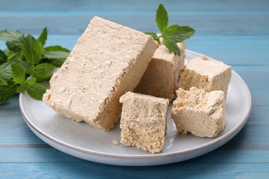 Pieces of tasty halva and mint on light blue wooden table, closeup