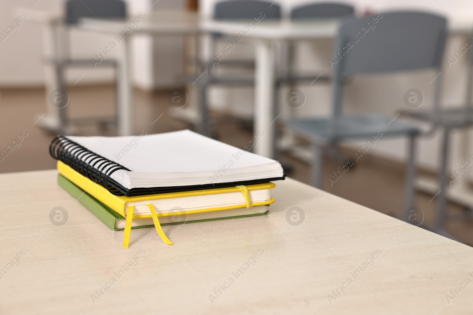 Photo of Stack of notebooks on wooden desk in empty classroom