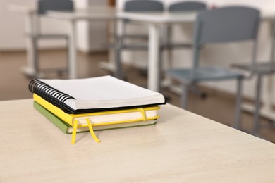 Stack of notebooks on wooden desk in empty classroom