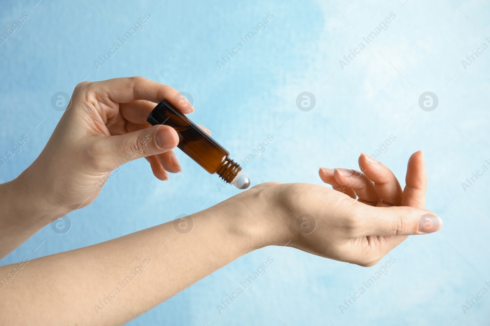 Photo of Woman applying essential oil on her wrist against color background, closeup