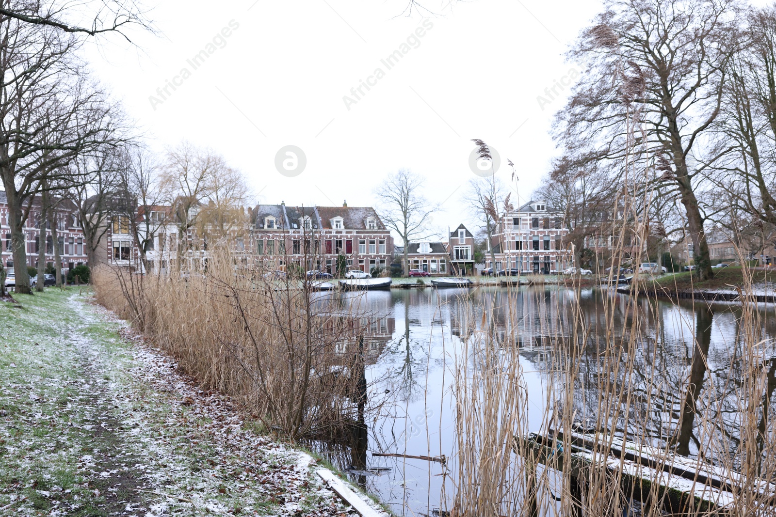 Photo of Picturesque view of water canal with moored boats, trees and buildings in city on winter day