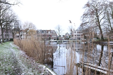 Picturesque view of water canal with moored boats, trees and buildings in city on winter day