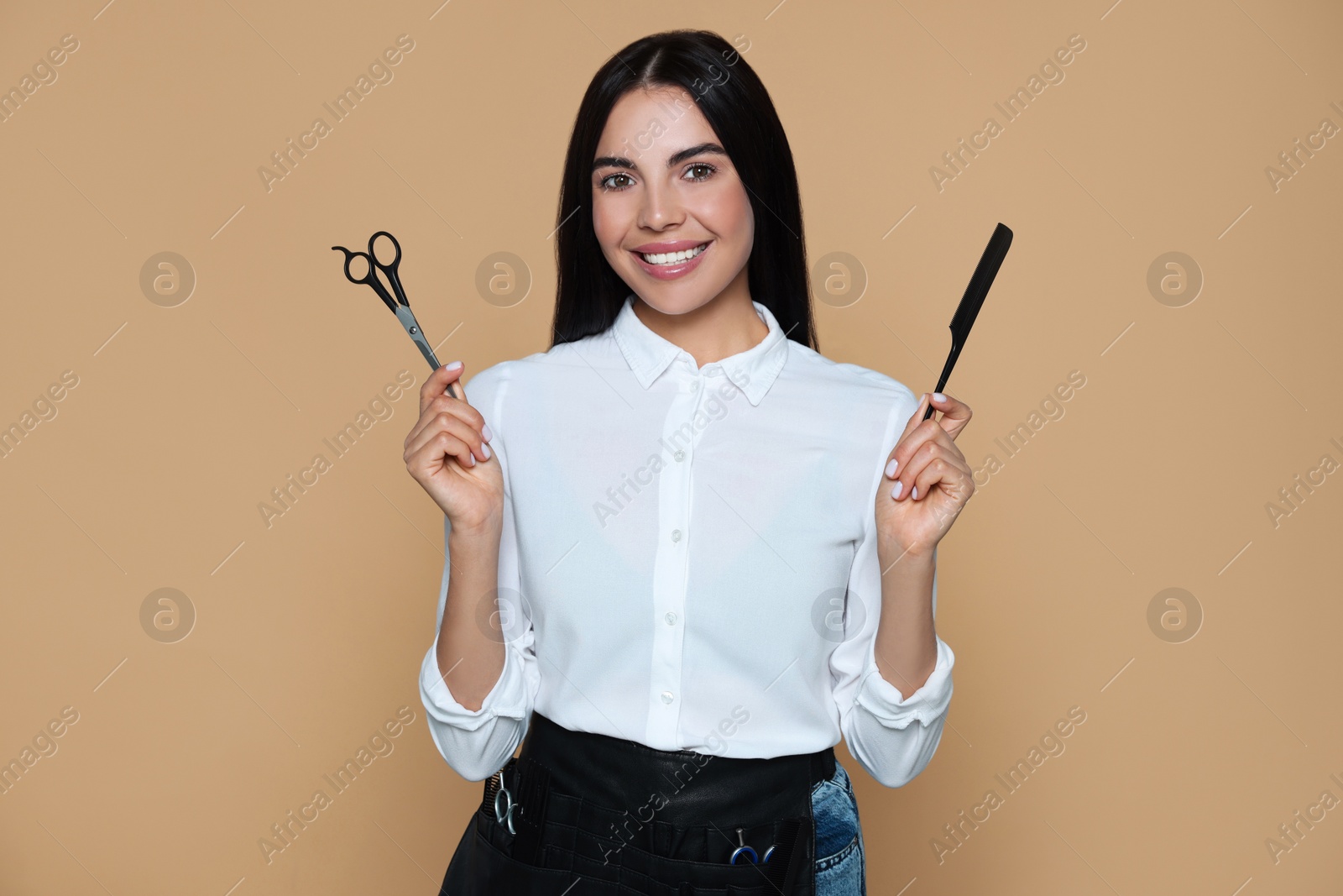 Photo of Portrait of happy hairdresser with professional scissors and comb on beige background