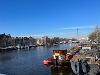 Photo of Amsterdam, Netherlands - March 01, 2023: Picturesque view of river embankment with moored boats in city under blue sky