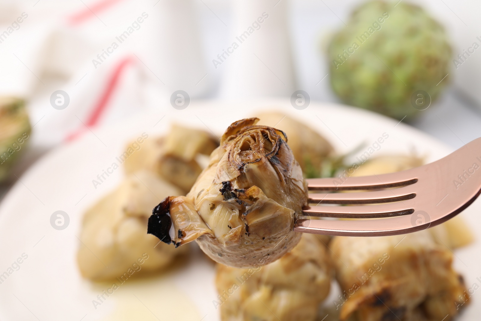 Photo of Fork with tasty pickled artichoke on blurred background, closeup view