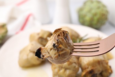 Fork with tasty pickled artichoke on blurred background, closeup view