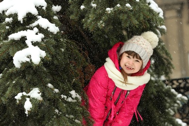 Little girl hiding under tree branches outdoors on snowy day