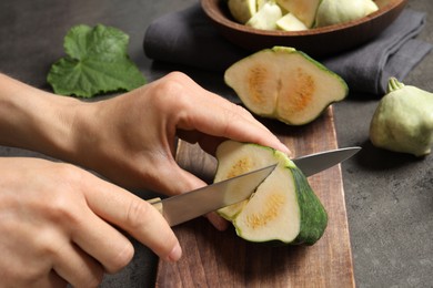 Photo of Woman cutting ripe green pattypan squash at grey table, closeup