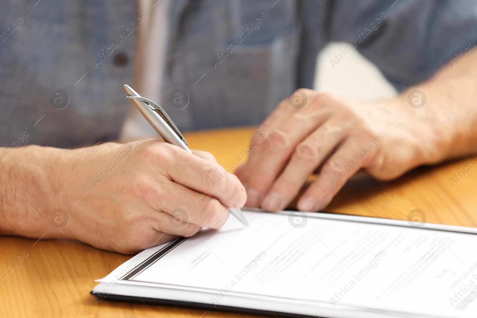 Photo of Senior man signing Last Will and Testament at wooden table, closeup