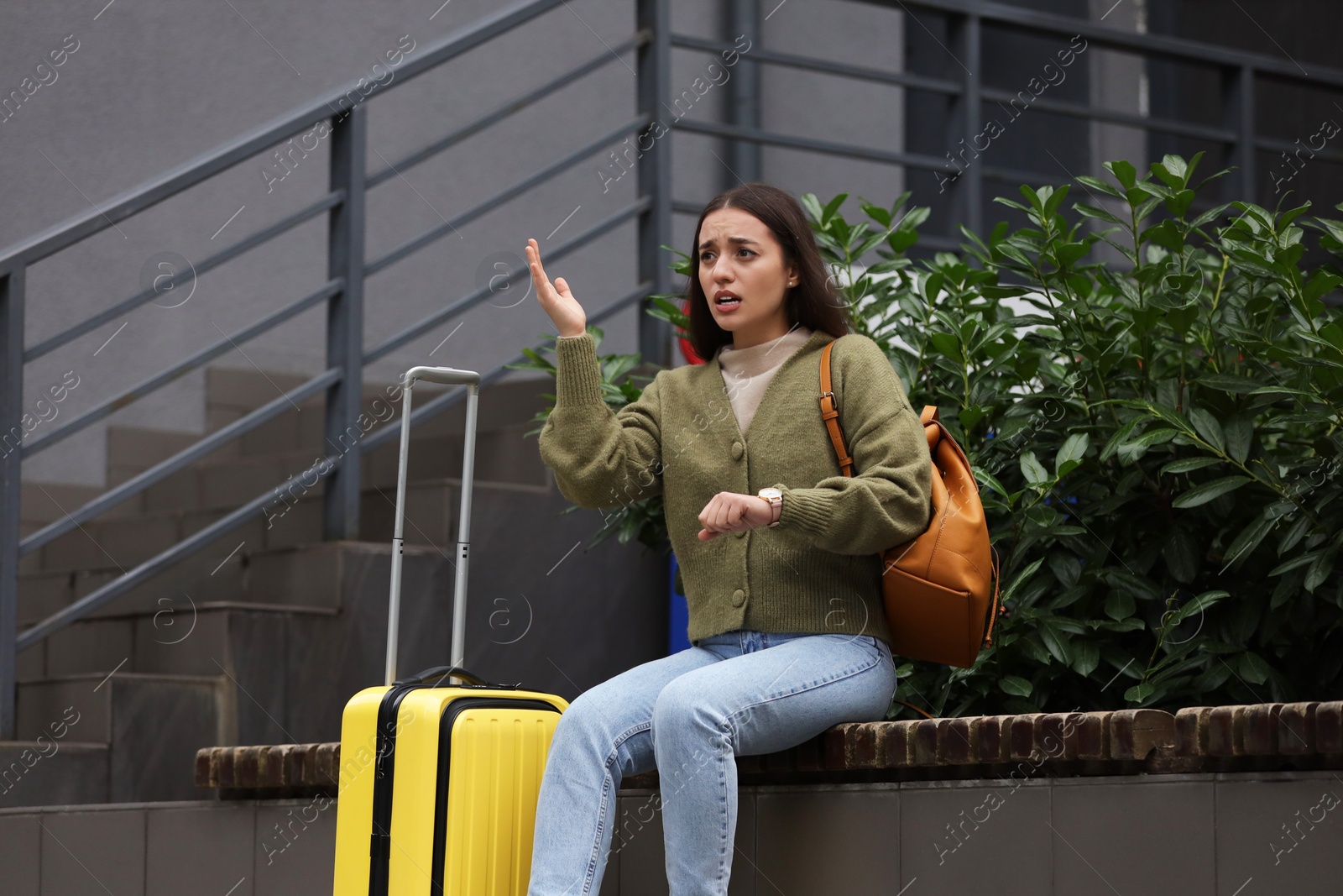 Photo of Being late. Worried woman with suitcase sitting on bench outdoors