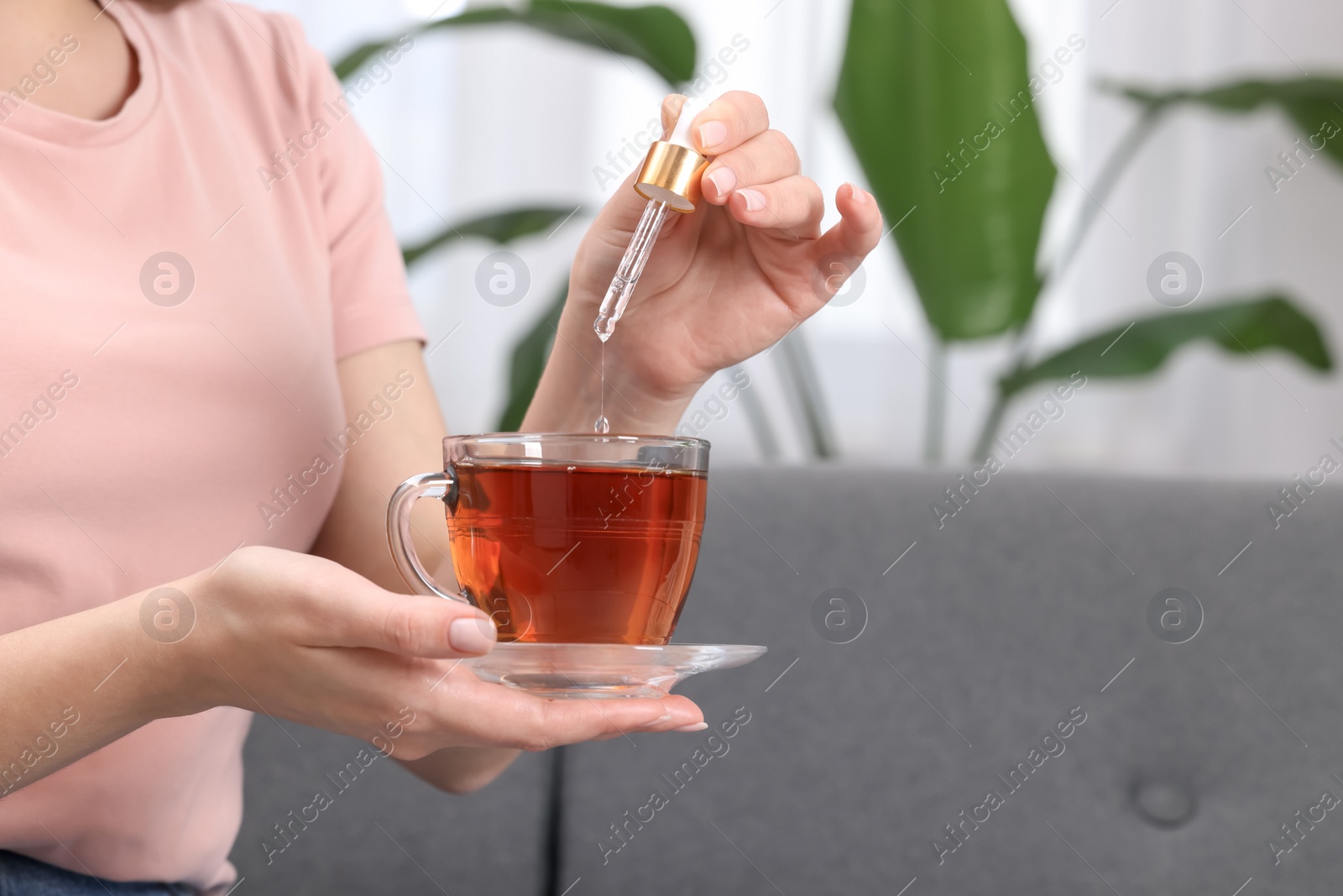 Photo of Woman dripping food supplement into cup of tea indoors, closeup. Space for text