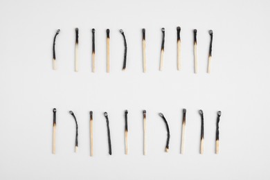 Different stages of burnt matches on white background, flat lay
