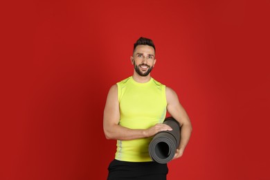 Photo of Handsome man with yoga mat on red background