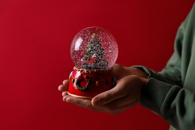 Photo of Man holding snow globe on red background, closeup