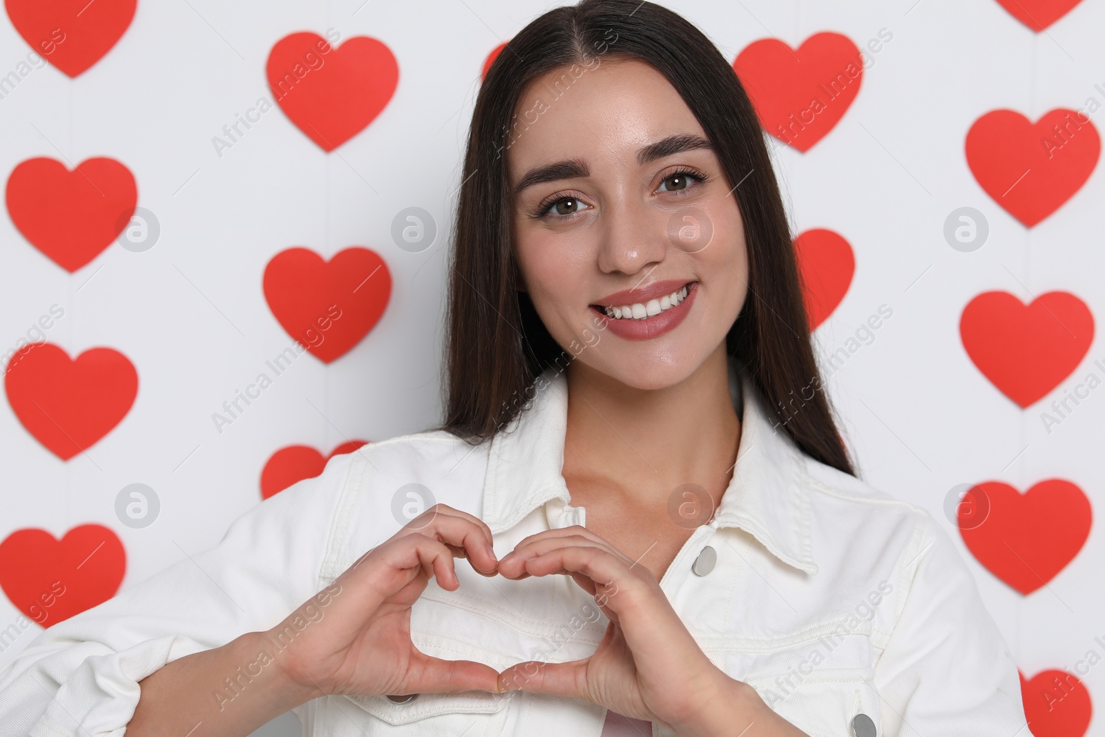 Photo of Happy young woman making heart with hands on decorated background