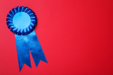 Photo of Blue award ribbon on red background, top view. Space for text