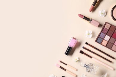 Photo of Flat lay composition with different makeup products and beautiful spring flowers on beige background, space for text