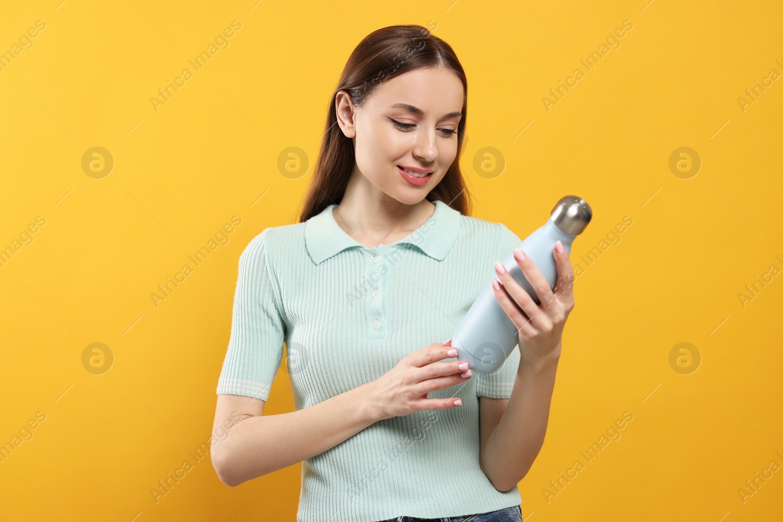 Photo of Beautiful young woman with thermos bottle on orange background