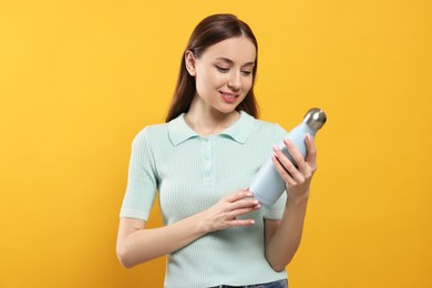 Beautiful young woman with thermos bottle on orange background