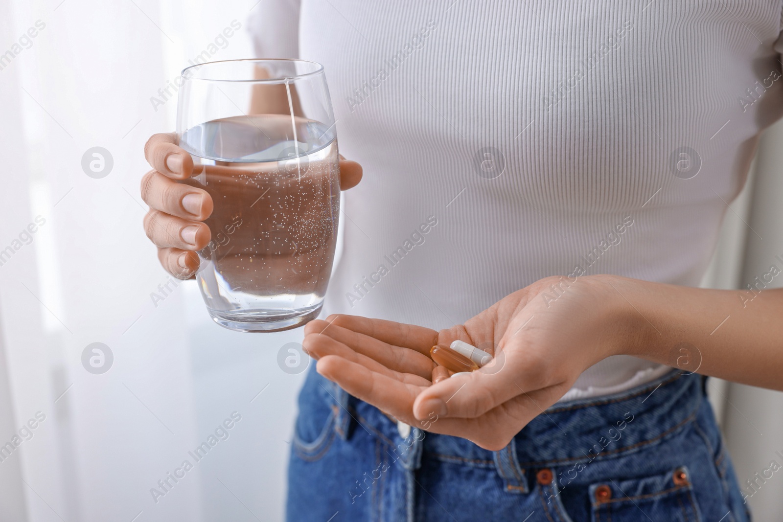 Photo of Woman with vitamin pills and glass of water indoors, closeup