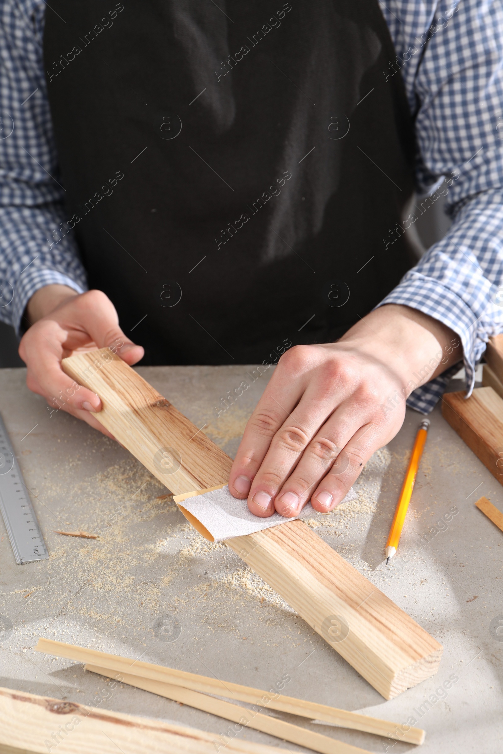 Photo of Man polishing wooden plank with sandpaper at grey table, closeup