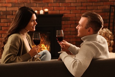 Happy lovely couple with glasses of wine spending time together near fireplace at home