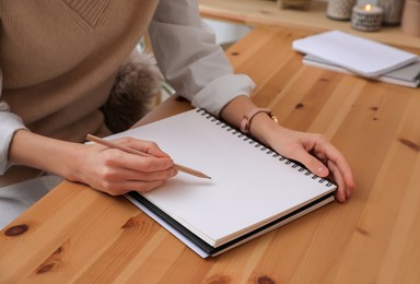 Woman drawing in sketchbook with pencil at wooden table indoors, closeup