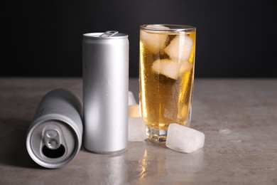 Photo of Tasty energy drink with ice cubes in glass and aluminium cans on grey table