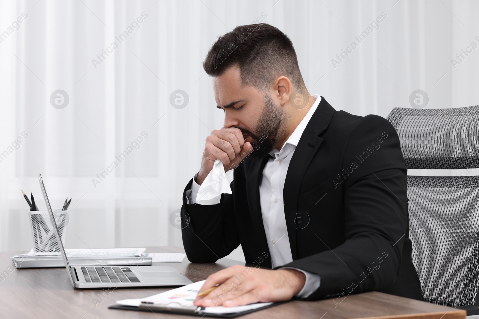 Photo of Sick man with tissue coughing at workplace in office